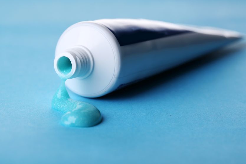 Tube with blue toothpaste on color background
